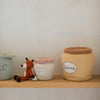 Three handcrafted Basket Honey Pots labeled "cookies," "strawberry jam," and "honey" on a shelf, next to a small knitted fox toy.