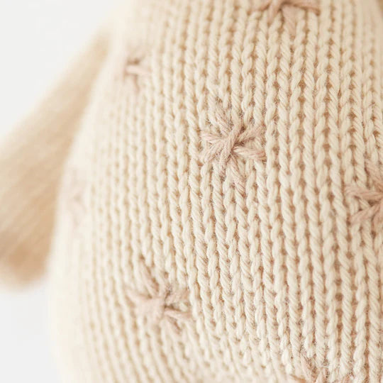 Close-up of a beige hand-knit fabric showing detailed stitch patterns and textures, crafted from Cuddle + Kind Baby Giraffe cotton yarn.