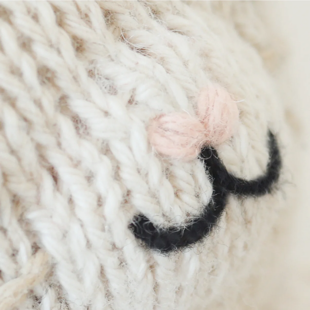 Close-up of Cuddle + Kind Baby Mouse’s cream-colored knitted fabric made from Peruvian cotton yarn, showing an embroidered black closed eye and two light pink blush knots above it.