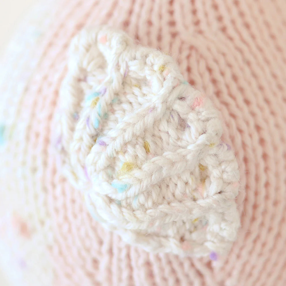 Close-up of a hand-knit piece made from natural Peruvian cotton yarn in powder pink, with a white textured pattern and pastel speckles. It likely displays cute baby animals, perhaps as part of the Cuddle + Kind Baby Seahorse (Powder Pink) garment or collectible accessory.