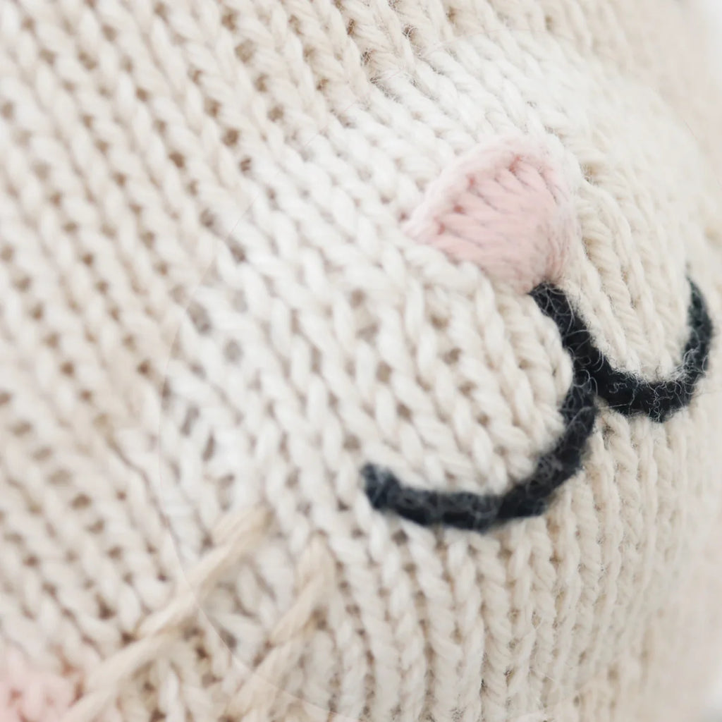 Close-up of Cuddle + Kind Bailey The Mouse, a cream-colored hand-knit doll with embroidered black lines like closed eyes and a pink ear, resembling a sleeping animal. Filled with hypoallergenic polyfill for comfort.
