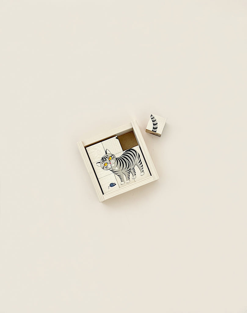 A Wooden Block Puzzle - 9 Piece Farm Animals standing beside a small matchbox with an illustrated zebra design on a plain beige background, made in Switzerland.