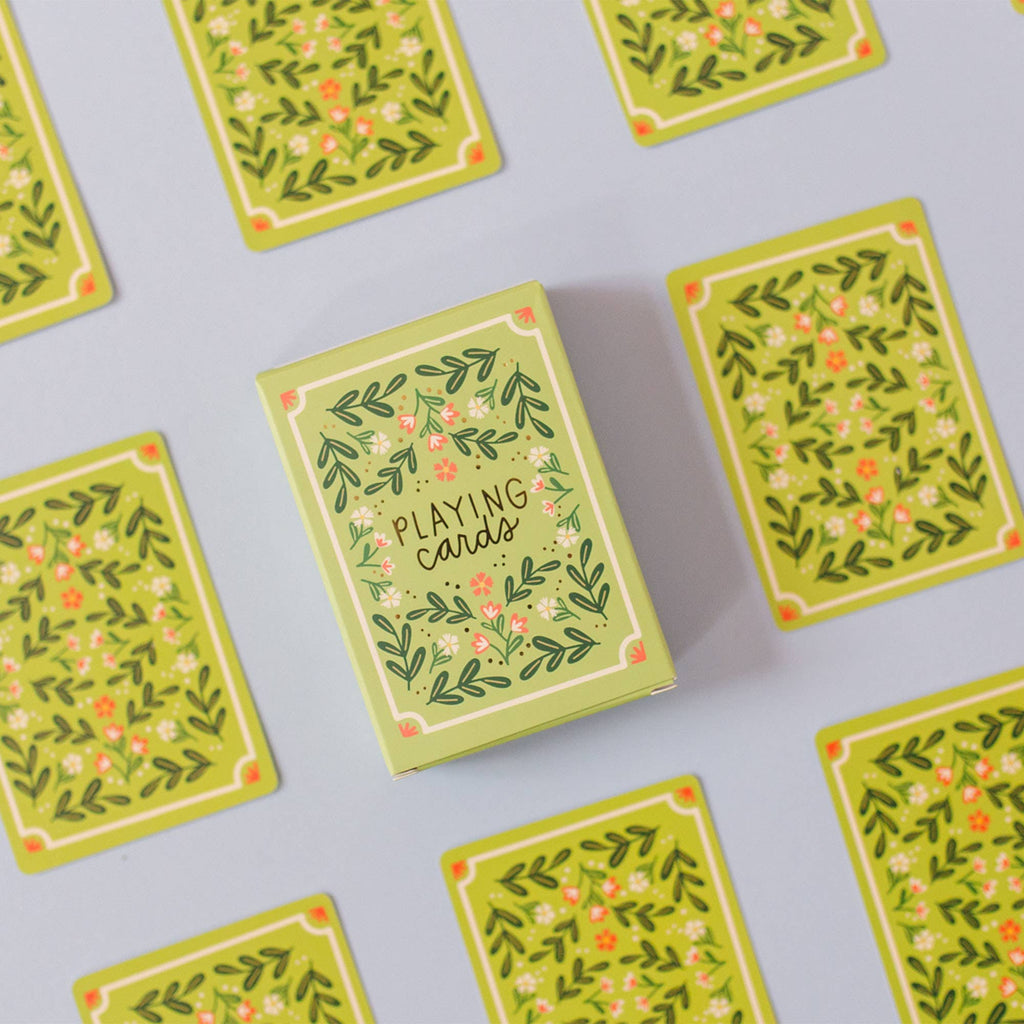 The Green Floral Deck of Playing Cards (ships in approximately one week), featuring elegant green hand-illustrated designs, is displayed with matching cards face down on a light surface—ideal for an elegant game night.