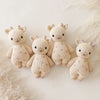 Four Cuddle + Kind Baby Giraffe dolls depicting plush giraffe toys with smiling faces, seated on a cream background. Each toy is hand-knit in a light beige color with small, printed hearts on their bodies.
