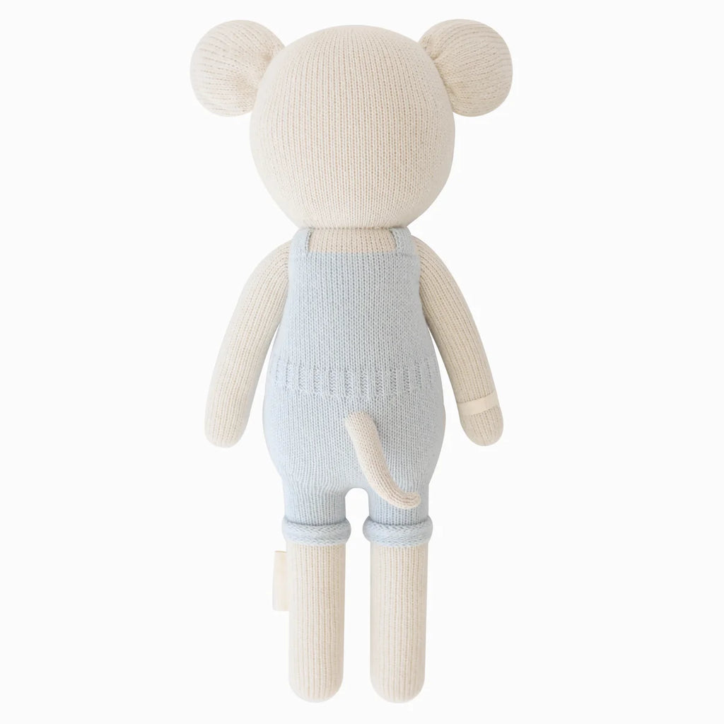 Cuddle + Kind Bailey The Mouse, a hand-knit cream-colored plush, is shown from the back in light blue overalls. Filled with hypoallergenic polyfill, it features round ears, a small tail, and stands against a plain white background.