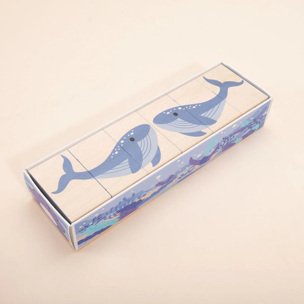 A coral reef puzzle with three wooden blocks that together depict an illustration of two blue whales. Made from sustainable basswood, the background of the Ocean Blocks box features an ocean-themed design with marine life. The blocks are neatly packed inside the box.
