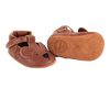 A pair of Donsje Baby Bear Shoes with a bear face design and a Velcro fastening strap, displayed against a transparent background.