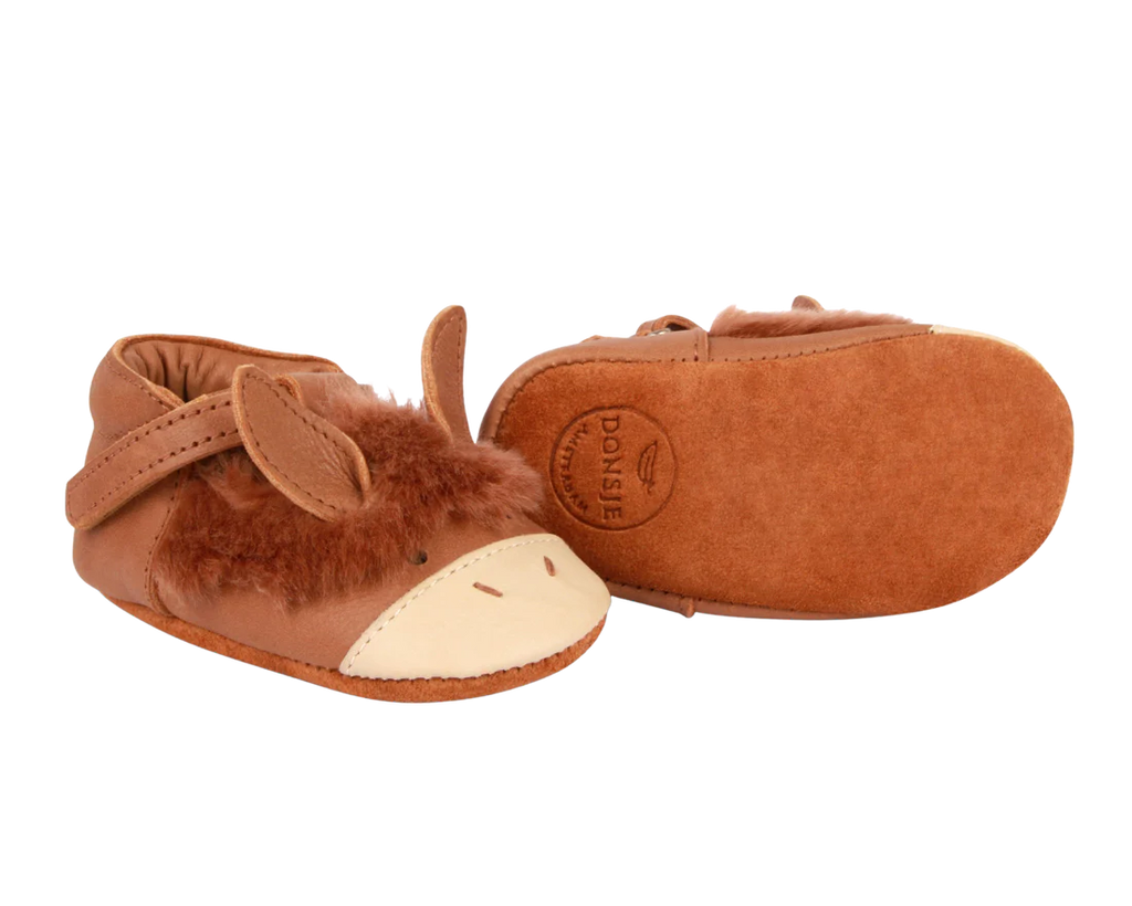 A pair of Donsje Baby Donkey Shoes designed to look like cartoonish brown horses, featuring soft materials, embroidered faces, and small ears with a Velcro fastening strap, isolated on a black background.