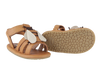 A pair of Donsje Baby Bee Shoes with tan straps, white petal-shaped embellishments, and a non-slip tan sole featuring a Velcro closure. The shoes are displayed against a white background.