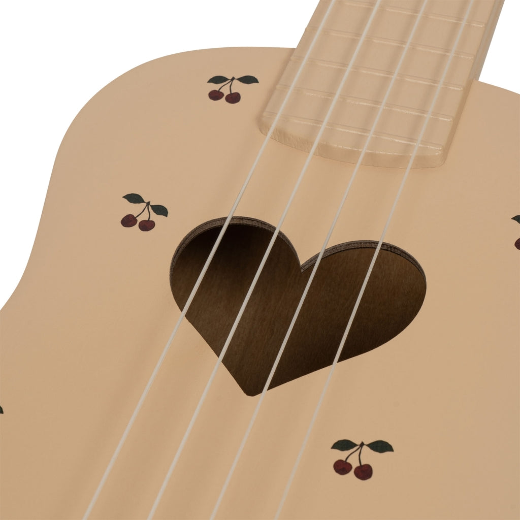Close-up of the Wooden Ukulele - Cherry, a light-colored instrument featuring a heart-shaped sound hole, small cherry illustrations on its body, and four visible strings.