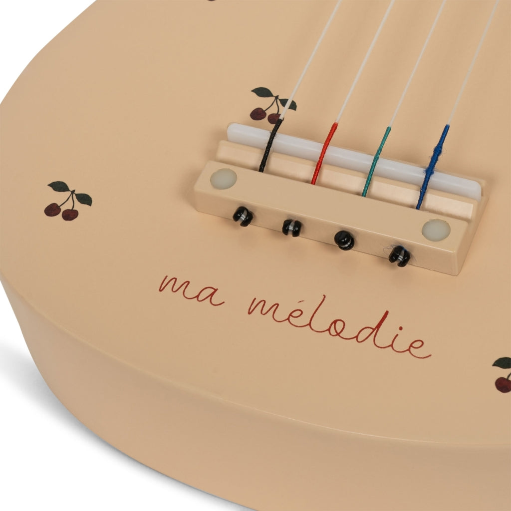 The Wooden Ukulele - Cherry features a cream finish, small cherry illustrations, and "ma mélodie" in red script, making this charming instrument a delightful choice for music lovers.