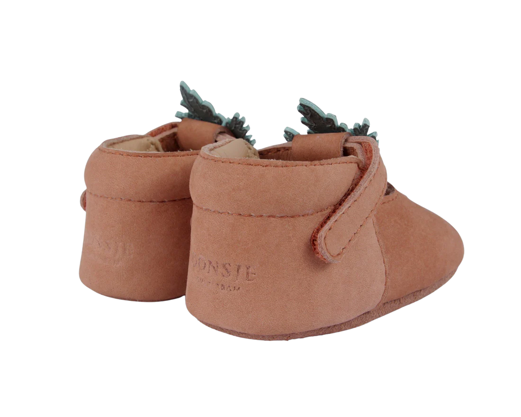 A pair of Donsje Baby Carrot Shoes, handmade from 100% premium leather, with decorative frills and a velcro strap, isolated on a black background.