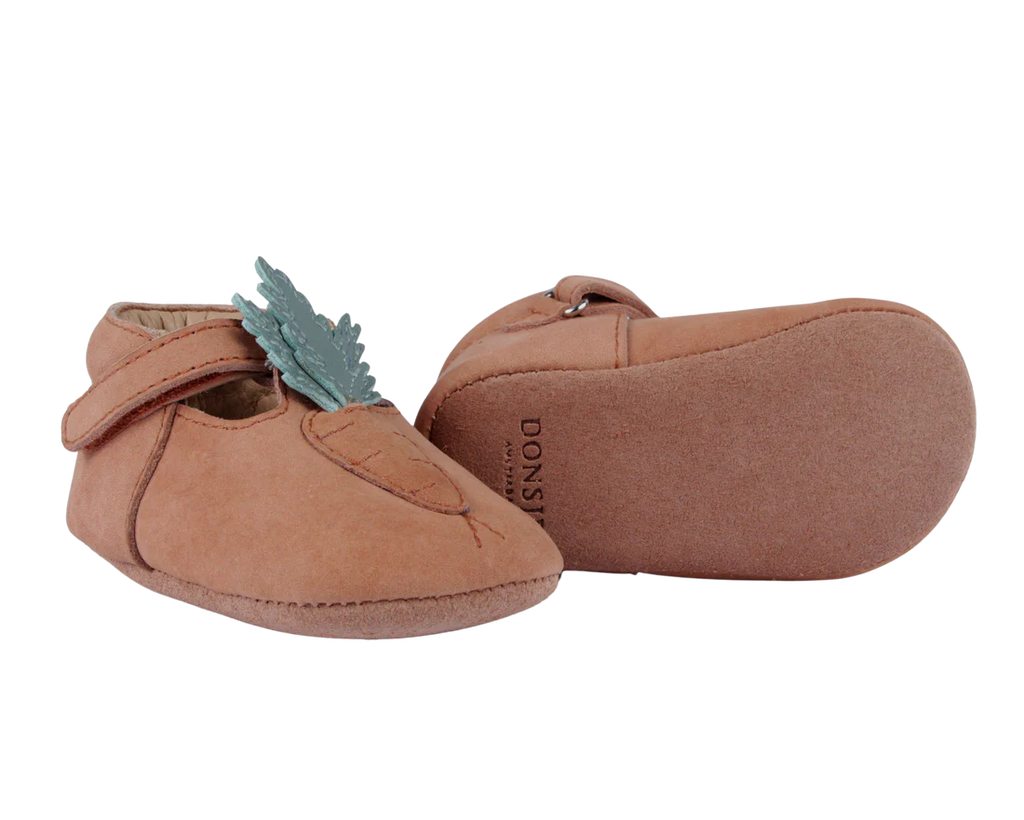 A pair of handmade fairtrade Donsje Baby Carrot Shoes with a Velcro strap and a decorative mint leaf on the side, against a transparent background.