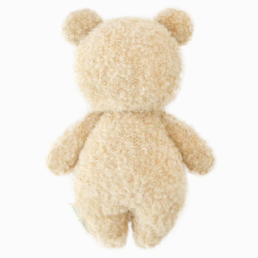 The Cuddle + Kind Baby Bouclé Bear - Honey is shown from the back, featuring soft beige Peruvian alpaca yarn, round ears, and no visible facial features against a plain white background.
