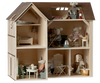 A detailed Maileg Farmhouse Dollhouse with four rooms and an attic, featuring furniture and mouse dolls engaging in various activities, like reading and cooking.