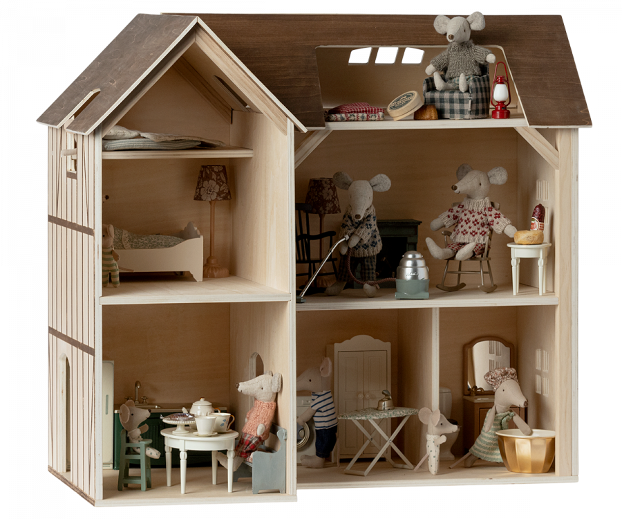 A detailed Maileg Farmhouse Dollhouse with four rooms and an attic, featuring furniture and mouse dolls engaging in various activities, like reading and cooking.