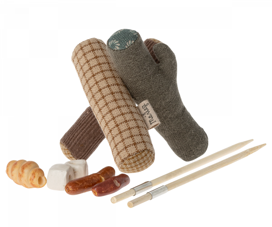 Various dog toys and treats, including a plaid cloth bone, a brown chew stick, and two wooden fetch sticks, displayed on a black background with Maileg Campfire accessories.