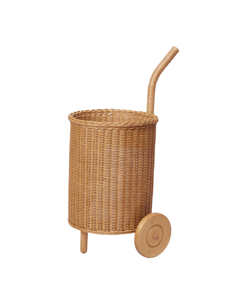 The Ferm Living Tukki Trolley - Natural, a cylindrical wicker rattan storage trolley with a curved handle and two wooden wheels, stands upright against a plain white background.