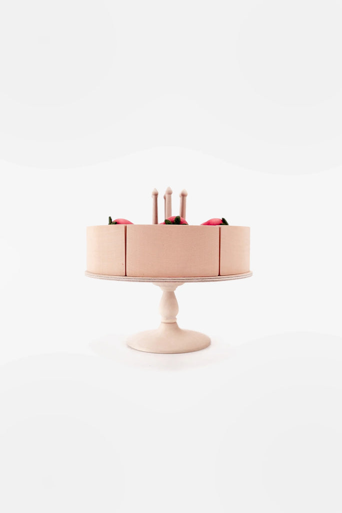 A minimalist-style birthday Handmade Strawberry Layer Cake On A Stand with pink frosting, three lit candles, and a few decorative berries, displayed on a white cake stand painted with non-toxic paint against a white background.