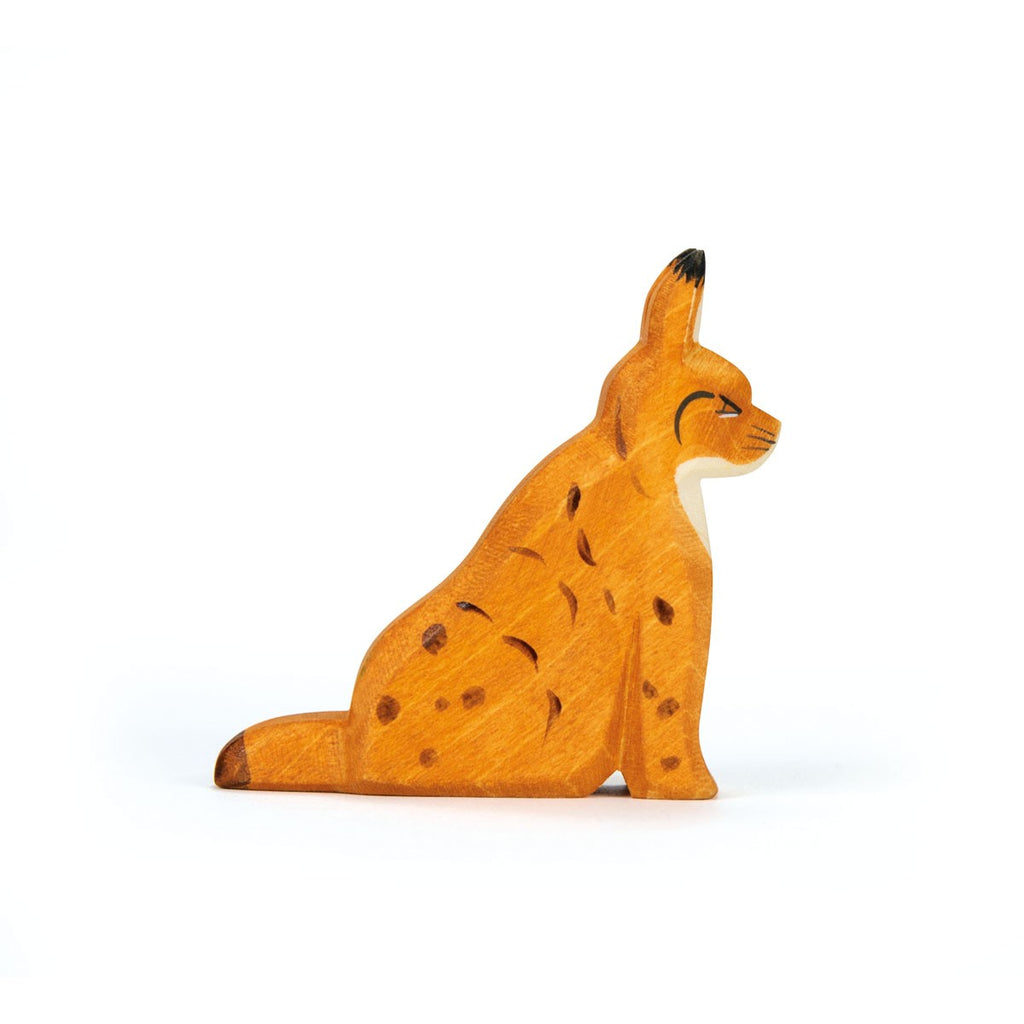 The Ostheimer Lynx Sitting is a handcrafted wooden figurine, painted orange with dark spots and markings, sitting upright with pointed ears and a short tail—perfect for imaginative play. Displayed against a plain white background.