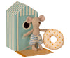 A small Maileg Beach Mouse - Little Brother wearing striped shorts holds a yellow polka-dotted inflatable ring. The mouse stands on a mat in front of a beach house with blue and white stripes, its circular entrance inviting vacation time.