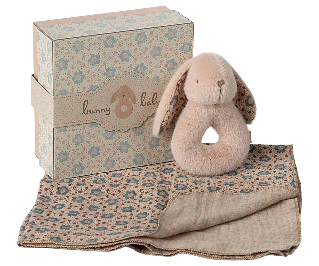 The Maileg Bunny Rattle Set - Powder is a charming gift featuring a plush bunny teether, a soft patterned baby blanket, and a delightful bunny rattle, all nestled in a decorative box with floral designs and the words "bunny baby," making it the perfect present for a little one.