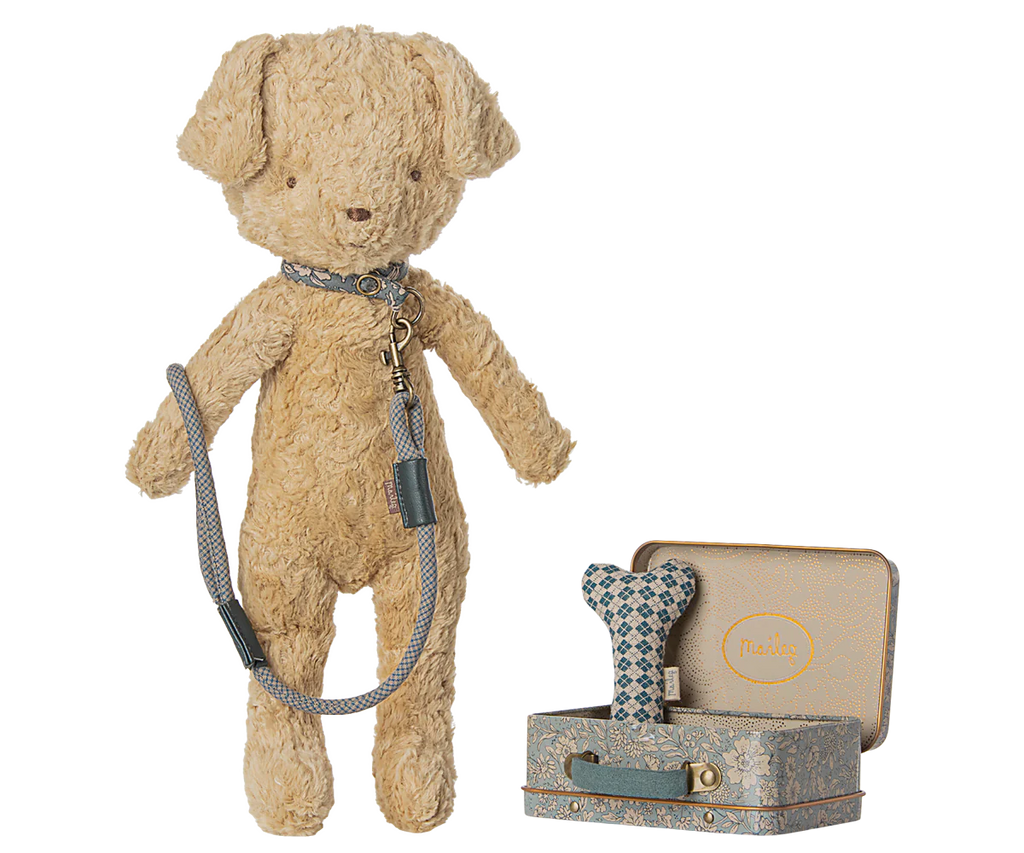 The Maileg Puppy Supply Accessories - Blue includes a soft plush dog with collar and leash, standing beside two metal suitcases—one open, one closed—with charming Maileg prints and a bone-shaped toy inside.