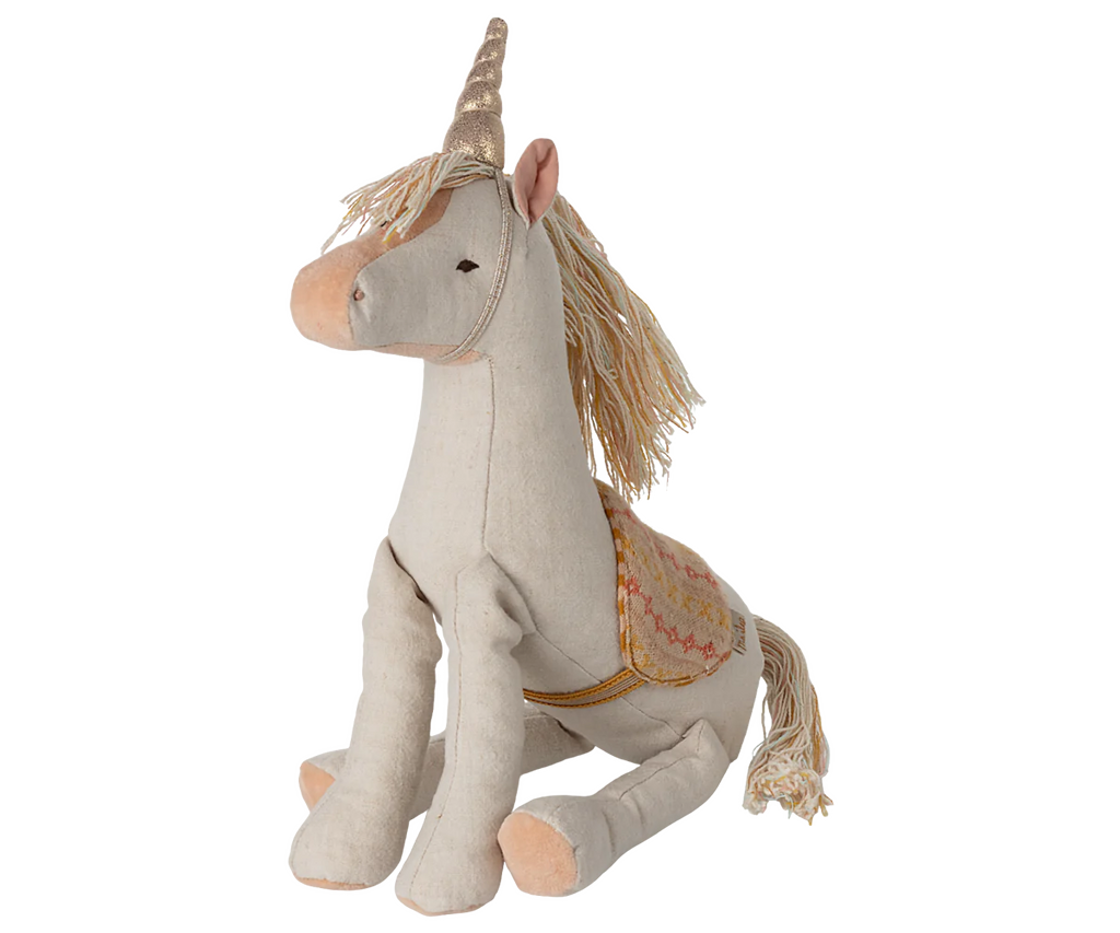The Maileg Unicorn, Medium is a plush toy made from linen-cotton with cream fabric, a gold horn, pink nose, and a decorative saddle, sitting upright against a striped pastel background.