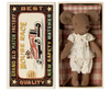A Maileg Big Sister, Mouse In Matchbox wearing white clothes lies inside an open matchbox bed. The matchbox has a vintage design with a colorful illustration of a car and text that reads "Grand Old Match Factory," "Best Quality," "Mouse Race," and "New Safety Matches." The tiny toy is surrounded by soft fabrics.