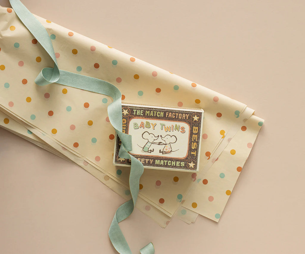 A pastel matchbox labeled "Baby Thing" with two elephants rests on polka-dotted gift wrap, paired with Maileg Ribbon - Dusty Mint (10m), all arranged against a beige background for an exclusive look.