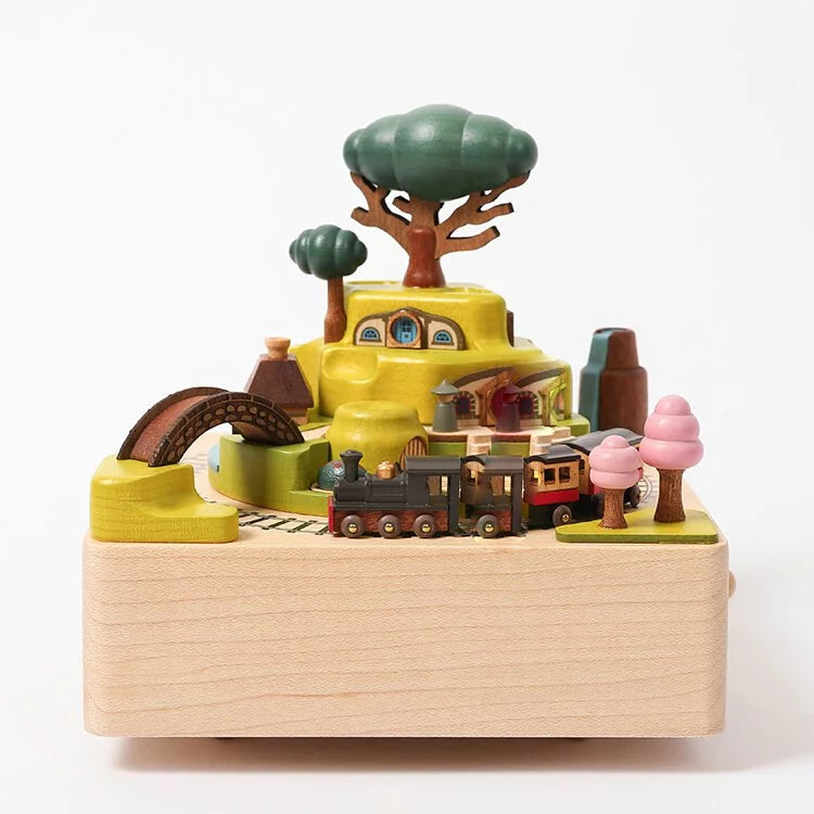 A Wooden Train Music Box - Spring toy set featuring a hand-cranked music box train on tracks, passing through a small village with buildings, trees, and a bridge, all crafted from sustainably sourced wood.