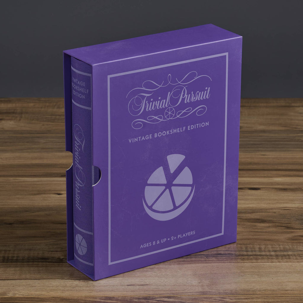 A purple box of Board Game: Trivial Pursuit Vintage Bookshelf Edition, styled like a classic book with white text and a pie graphic, rests on a wooden surface—an ideal addition to any Trivial Pursuit collection.