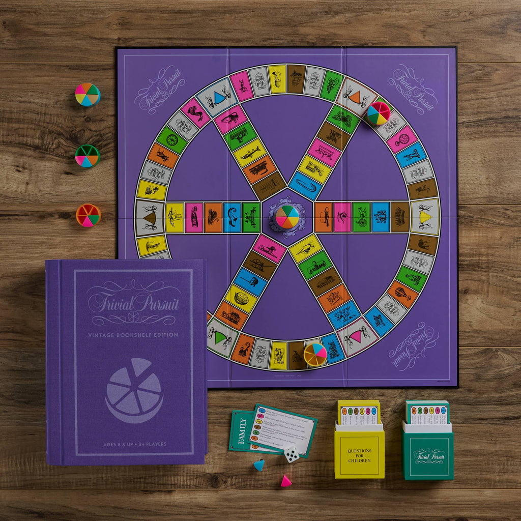 The Board Game: Trivial Pursuit Vintage Bookshelf Edition is displayed on a wooden table, showcasing its vibrant board, colored pieces, question cards, and unique purple book-shaped box.