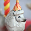 Close-up of a whimsical collectible Poodle Cake Topper figurine of a white poodle wearing a colorful striped party hat.