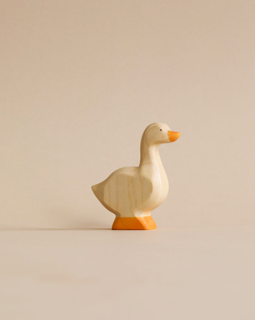 A Handmade Holzwald Goose carving with a smoothly polished surface, standing on a plain beige background. The goose is depicted in mid-stride with its head held high.