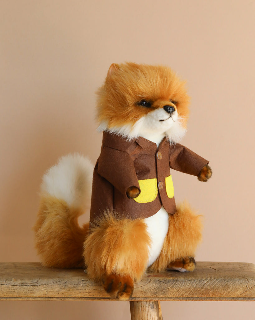 The Fox With Brown Jacket Stuffed Animal is a unique handcrafted toy, featuring a cute, fluffy fox in a brown jacket with yellow accents. It sits on a wooden surface against a beige background.