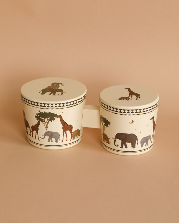Two Konges Sløjd Wooden Bongo Drums - Safari, decorated with silhouetted animals like elephants and horses, positioned on a soft beige background of FSC-certified beech wood.