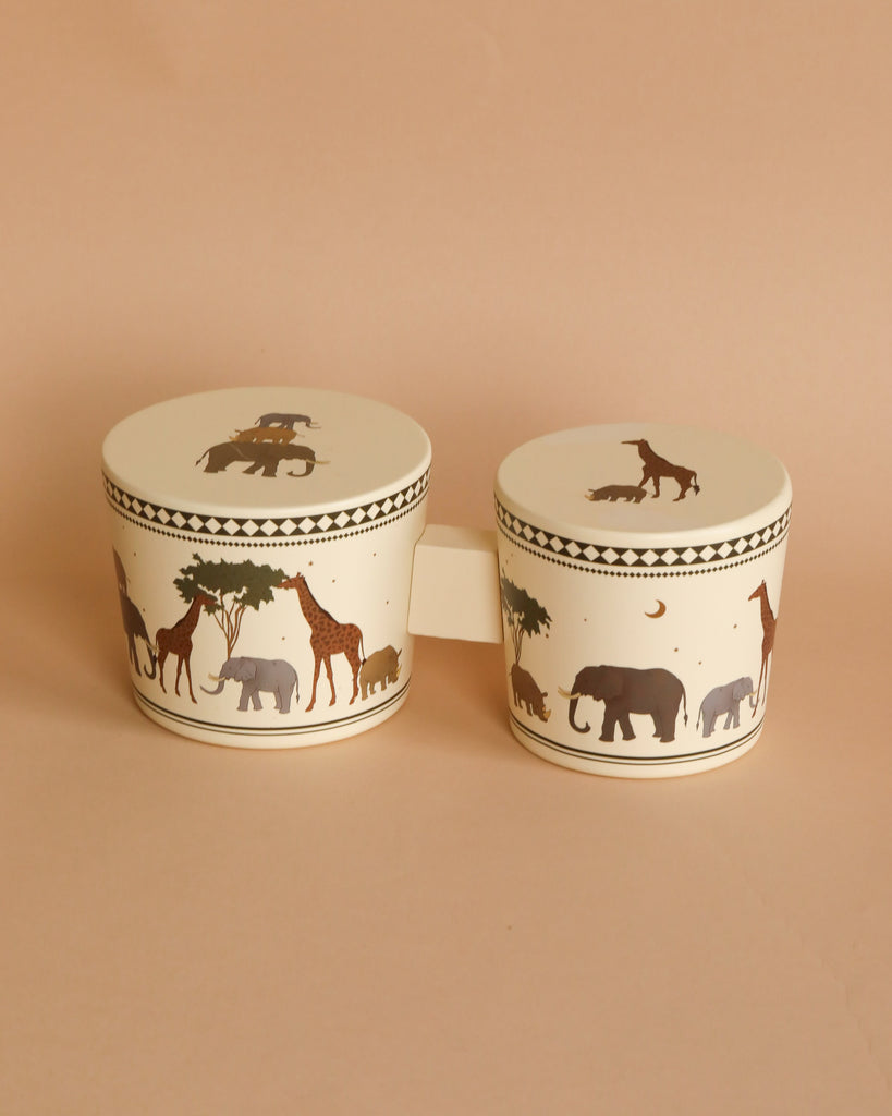 Two Konges Sløjd Wooden Bongo Drums - Safari, decorated with silhouetted animals like elephants and horses, positioned on a soft beige background of FSC-certified beech wood.