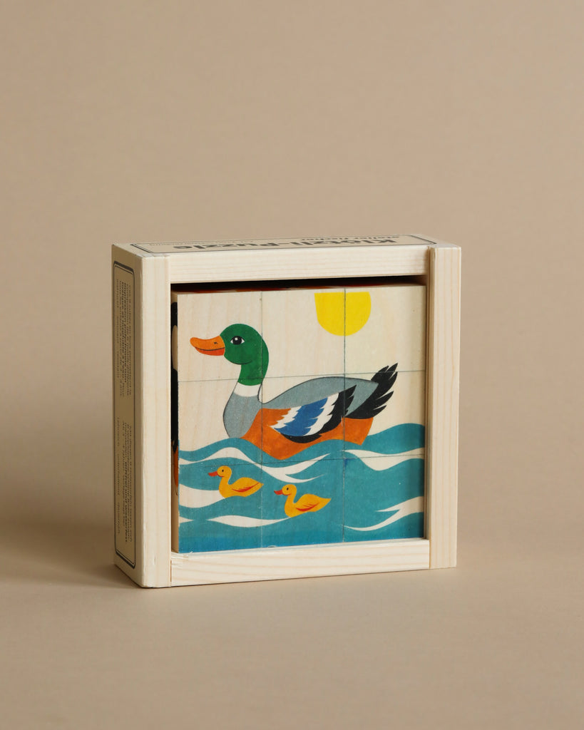 A Wooden Block Puzzle - 9 Piece Farm Animals featuring a colorful painting of a duck floating on water, with the sun in the background, showcased on a beige surface.