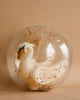 A Inflatable Swan Beach Ball with golden accents encapsulated in a translucent, glitter-filled snow globe against a beige background, composed of durable PVCD.