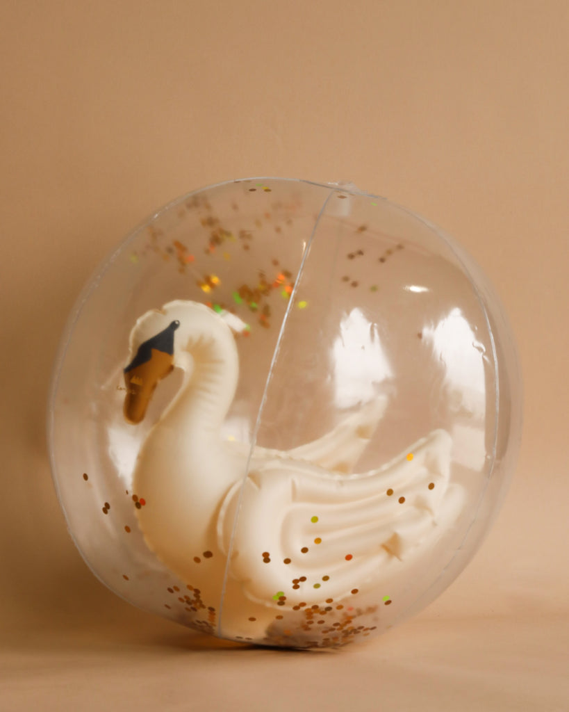 A Inflatable Swan Beach Ball with golden accents encapsulated in a translucent, glitter-filled snow globe against a beige background, composed of durable PVCD.
