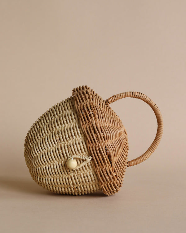 A handwoven Olli Ella Rattan Acorn Bag shaped like a fish, featuring intricate details and a small clasp, set against a soft beige background.