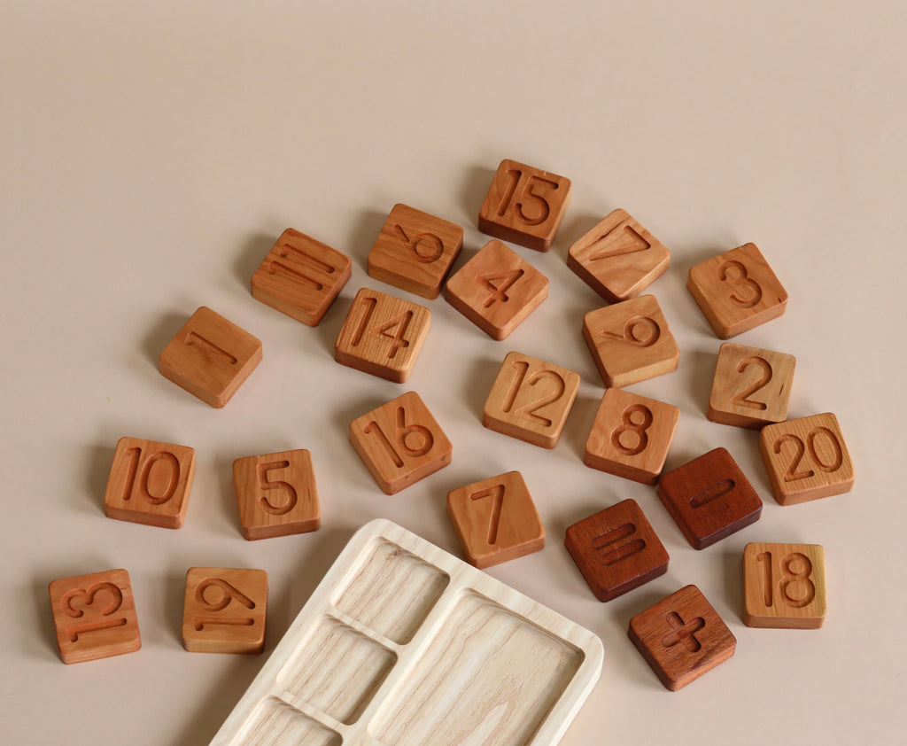 The Original Wooden Math Board - Made in USA made in USA with different numbers scattered on a beige surface, alongside an empty compartmentalized tray. The natural tones of the blocks showcase the wood grain.