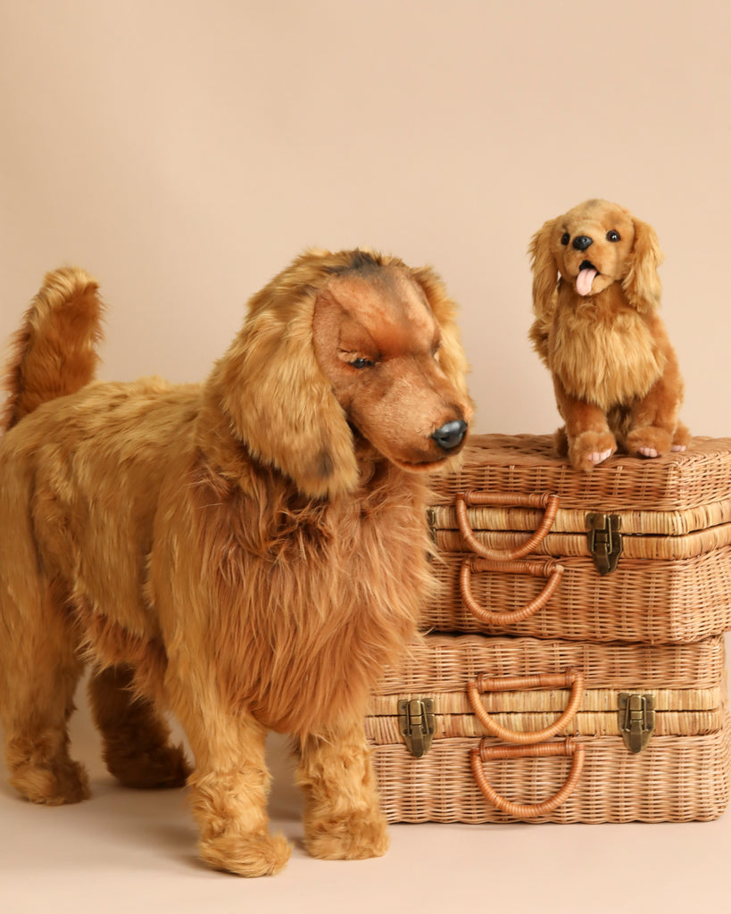 Two FINAL SALE - Life-size Golden Retriever stuffed toy dogs, a larger one standing in front and a smaller one sitting on top of two stacked wicker suitcases. Both golden retriever-like in appearance with fluffy golden fur and realistic features, these hand-sewn animals are set against a plain beige background.