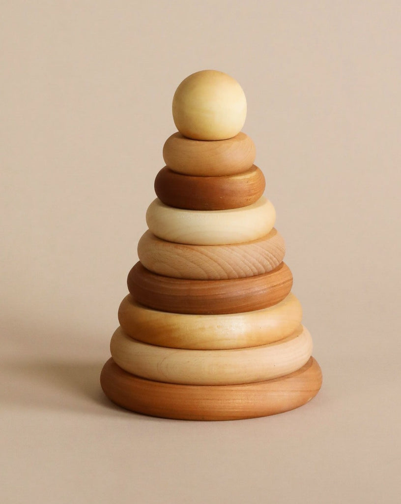 A wooden stacking toy with wooden rings in various natural shade of wood, stacked from large to small, topped with a sphere shaped wooden piece.