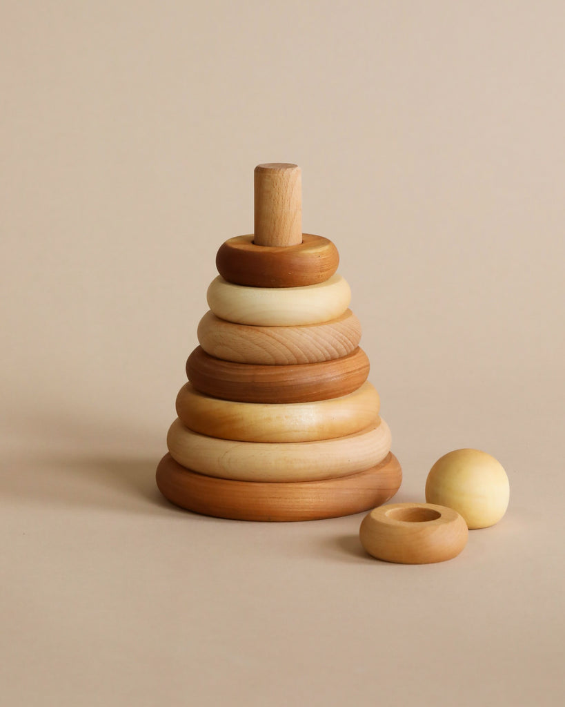 A wooden stacking toy with wooden rings in various natural shade of wood, stacked from large to small, topped with a sphere shaped wooden piece. 