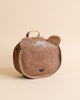 A brown Donsje School Leather Backpack - Bear designed to resemble a teddy bear's face, featuring rounded ears and simple facial features, set against a plain beige background.