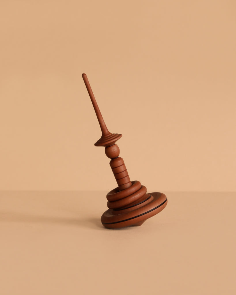 The Mader Apple Helene Top with Spinning Rings, crafted from apple wood, rests at an angle on a beige surface against a matching beige background.