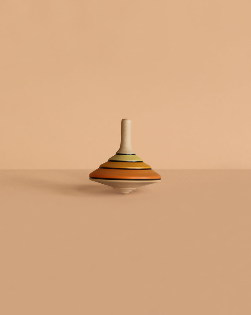 The Mader Tango Spinning Top - Orange, handcrafted from Maple wood and featuring orange stripes, rests on a smooth beige surface against a matching beige background.