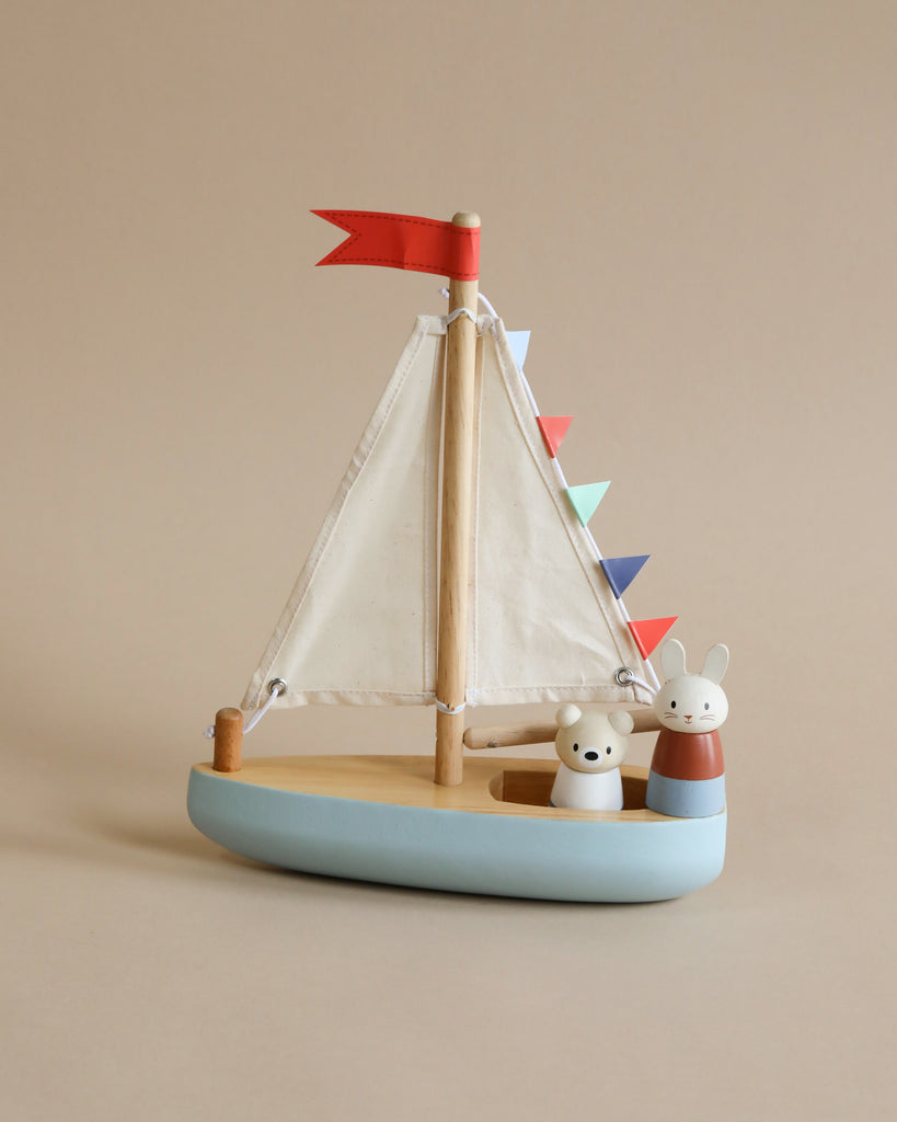 A colorful Wooden Sail Boat with fabric sails, featuring a blue base and multi-colored triangle flags. Two cute animal figures, a bear and a mouse, peek out from inside the boat.